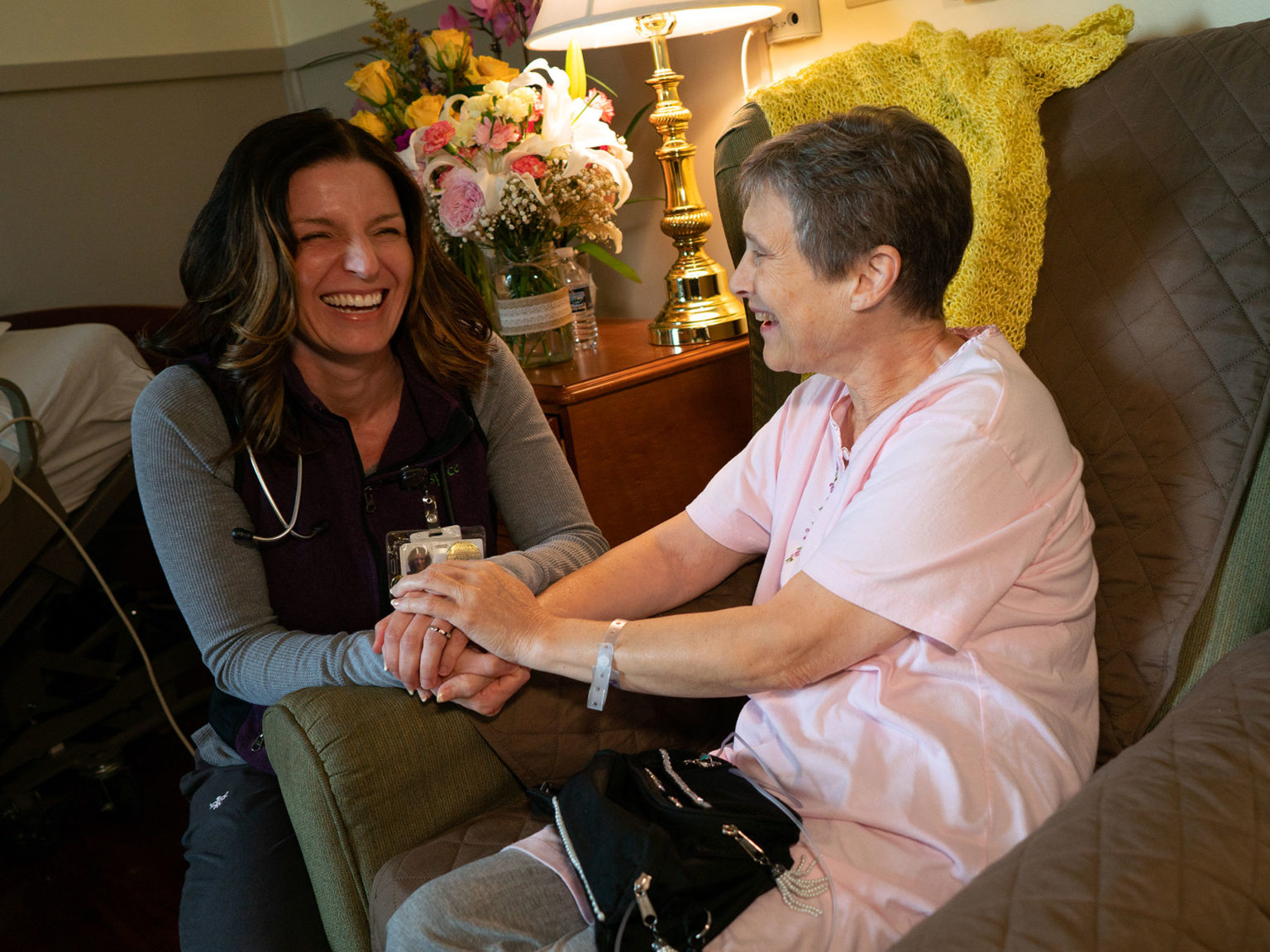 Older woman holding hands with female nurse at hospice facility